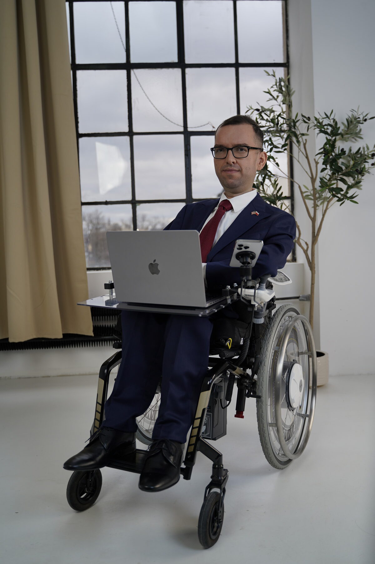 Adrian Furman przy laptopie, w wózku, w przestrzeni biurowej z dużym oknem